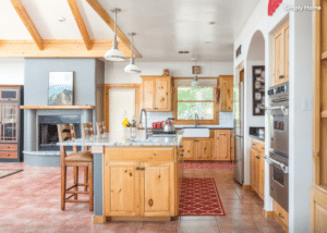 Rustic kitchen with wooden cabinets and an island, pendant lights, and a fireplace area to the left.