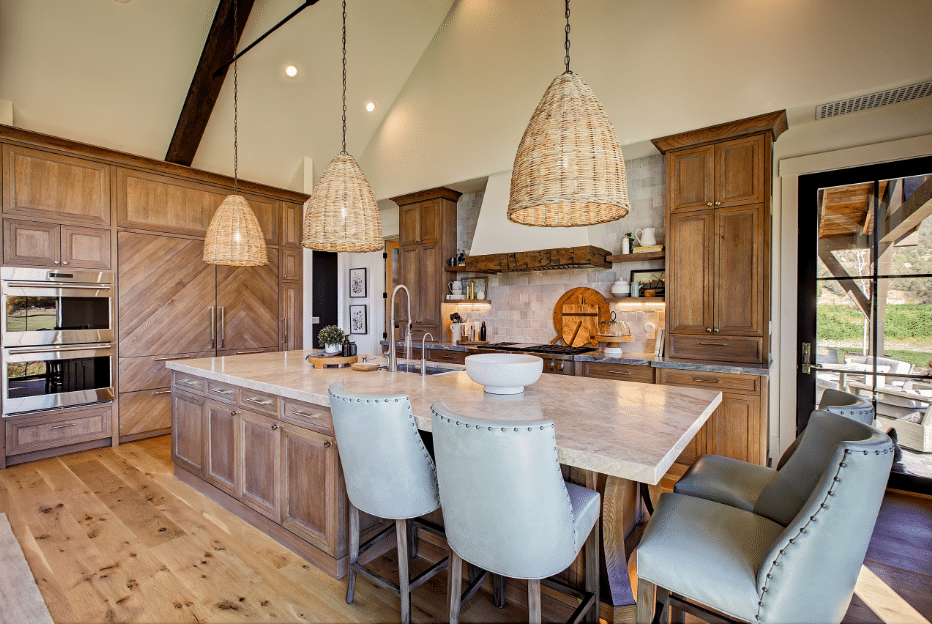 Rustic kitchen with a large marble island, wooden cabinets, and three woven pendant lights.