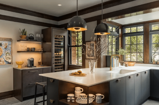 Modern kitchen with dark cabinets, white island, and pendant lights over a sunny windowed space, open shelving on the left.