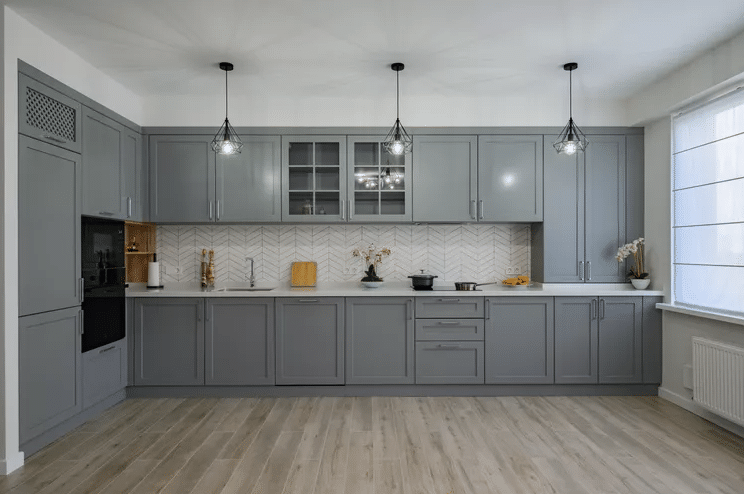 Modern grey kitchen with upper and lower cabinets, three pendant lights, and a light wood floor
