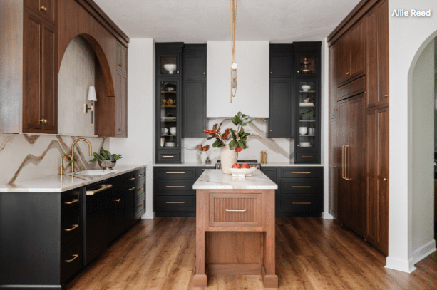 Modern kitchen with black and wood cabinets, marble countertops, and a central wooden island with a plant centerpiece.