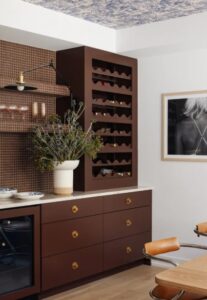 Brown wine rack and drawers in a modern kitchen, with a potted plant, mosaic backsplash, and a framed black-and-white photo on the wall.